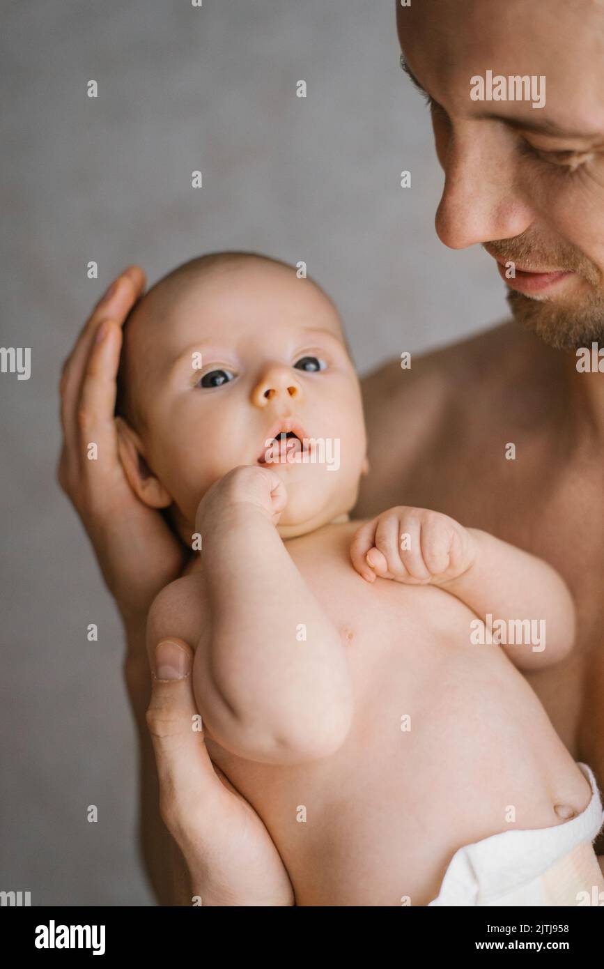 Feliz padre caucásico sostiene a su bebé en sus brazos y lo mira con cuidado y amor Foto de stock