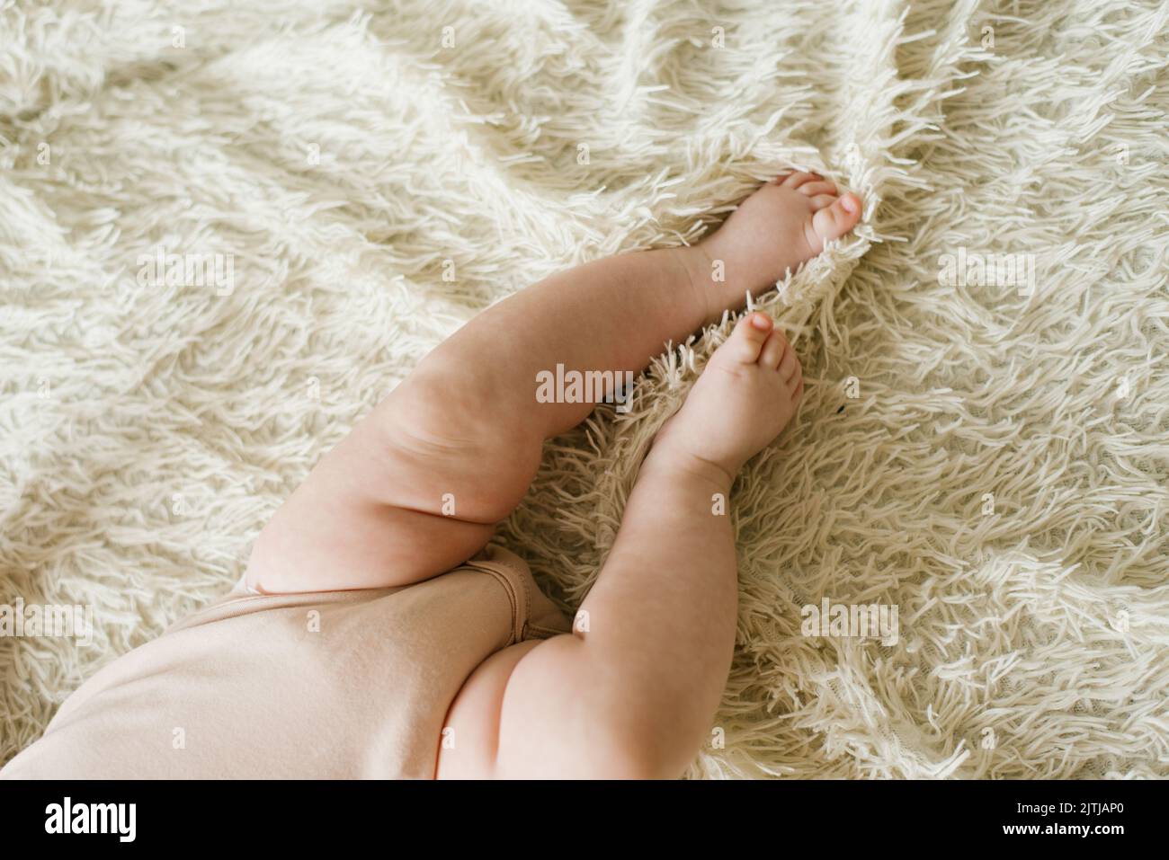 Vientre y piernas de un bebé recién nacido en un pelele acostado en una cama ligera, vista superior Foto de stock