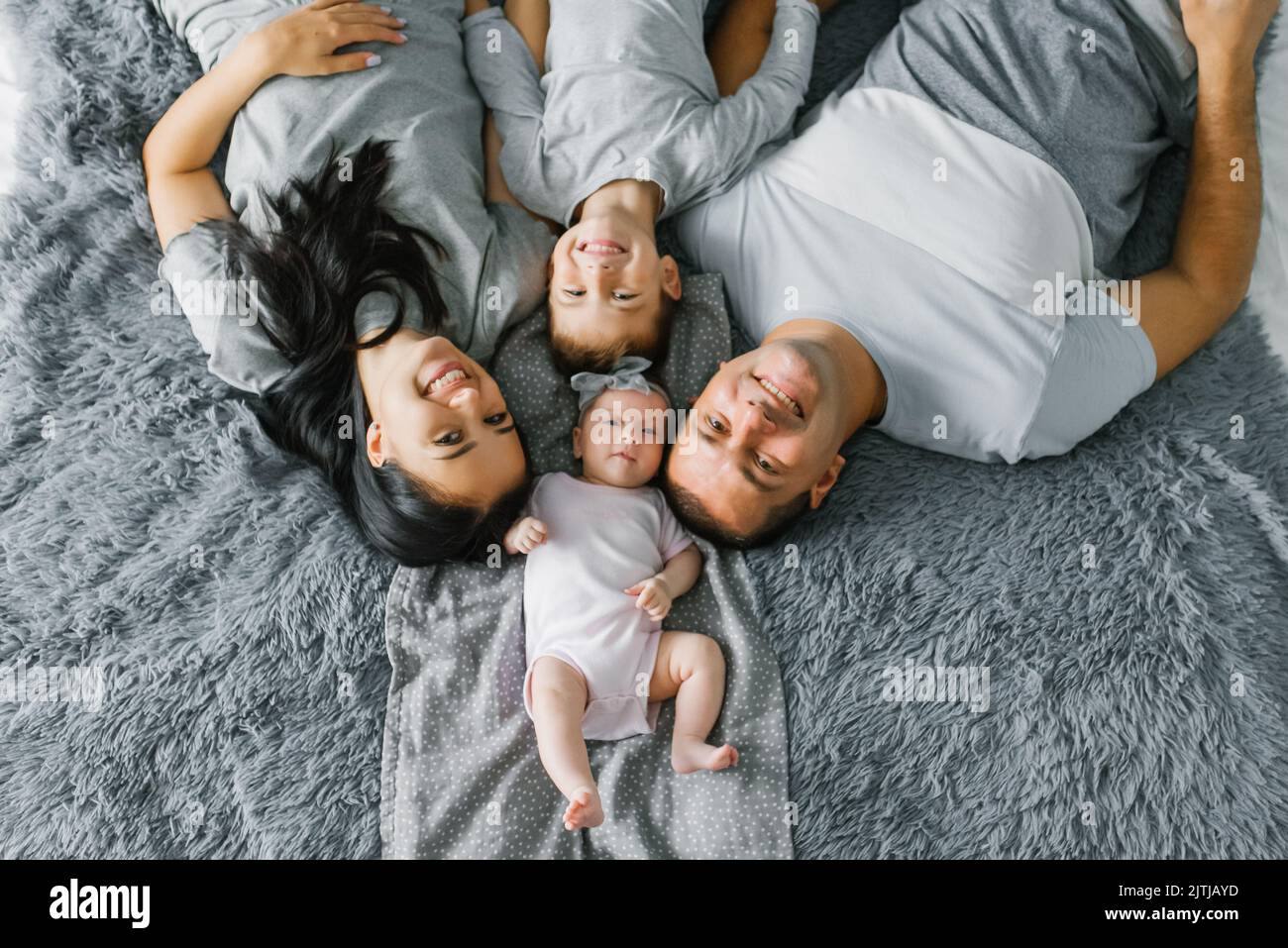 Una familia feliz con dos niños pequeños están tumbados en la cama y sonriendo. Vista superior Foto de stock