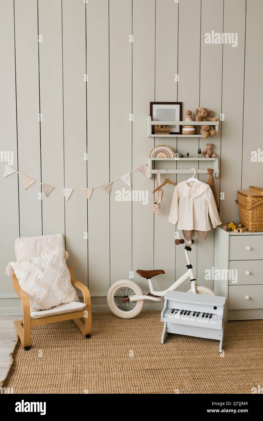 Elegante composición de un acogedor interior escandinavo de una habitación de niños con un sillón, peluche y juguetes de madera, una cesta de ratán en el pecho de Draw Foto de stock