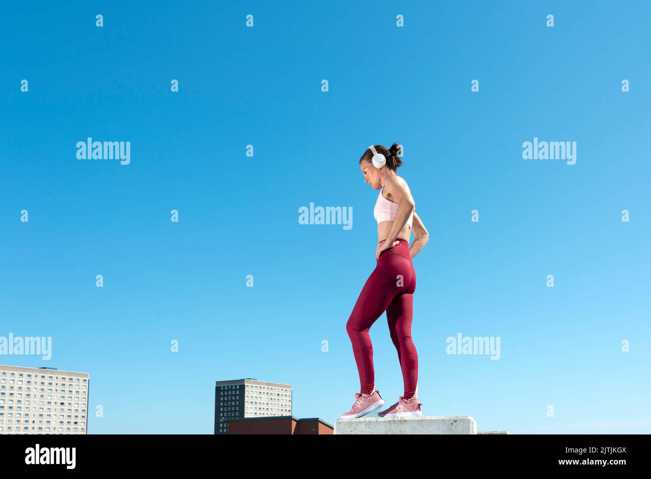 Mujer deportiva con auriculares de pie con las manos en las caderas. Entorno urbano. Foto de stock