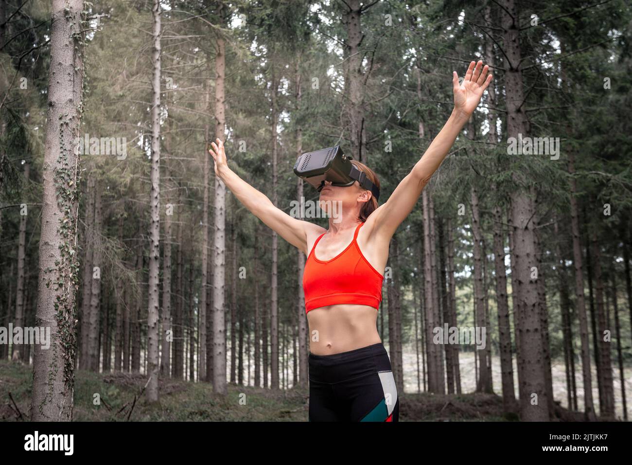 Mujer deportiva con auriculares Virual Reality haciendo ejercicio en un bosque virtual. Foto de stock