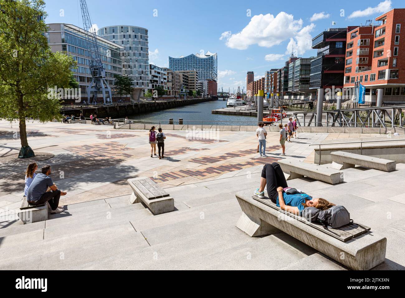 La gente se sienta en las terrazas Magellan bajo el sol del verano y contemple la Elbphilharmonie y la Hafencity de Hamburgo, Hamburgo, Alemania Foto de stock