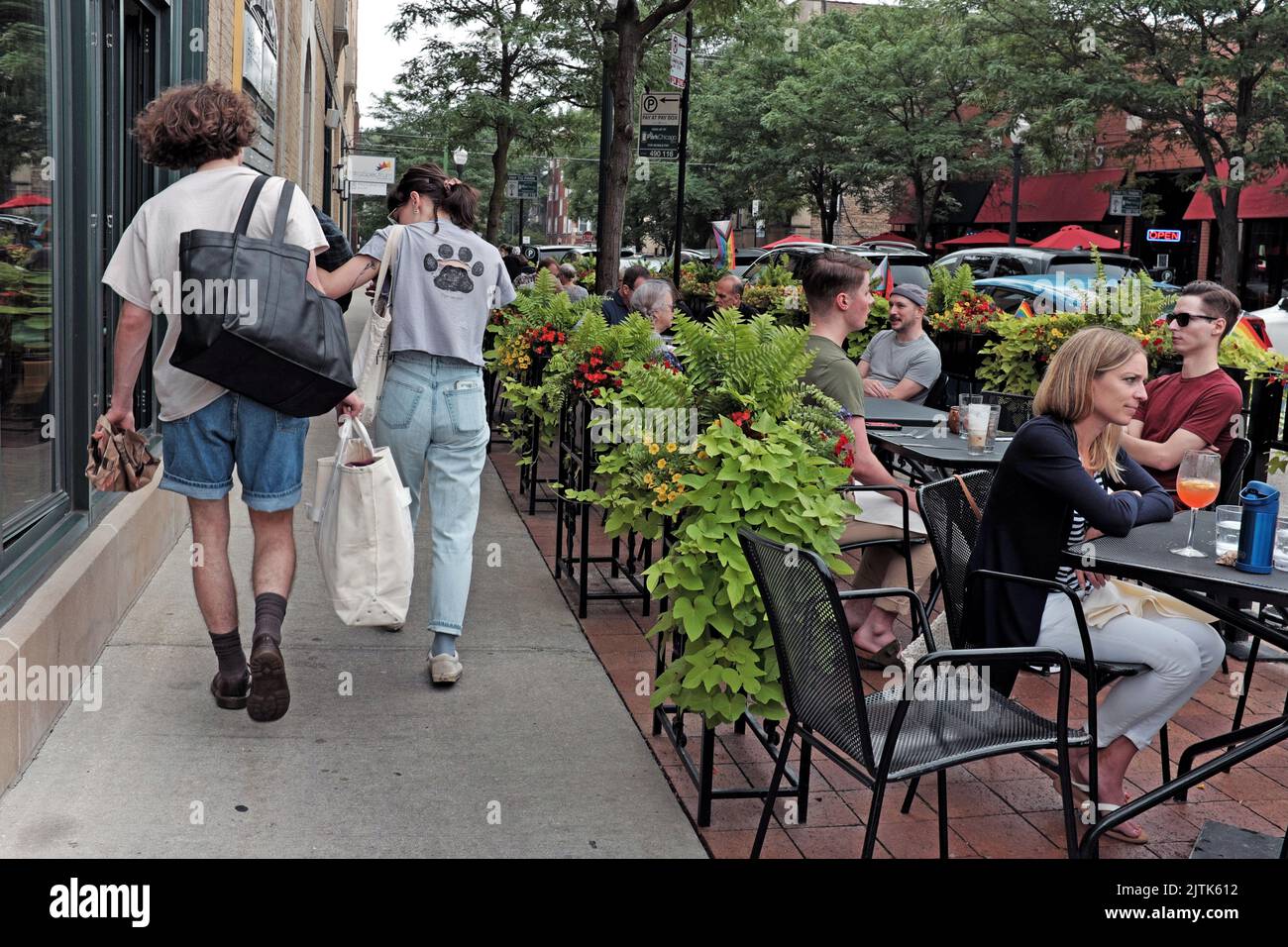 La gente cena afuera durante una tarde mientras los peatones caminan por la acera en el vecindario Andersonville en Chicago, Illinois, EE.UU. Foto de stock