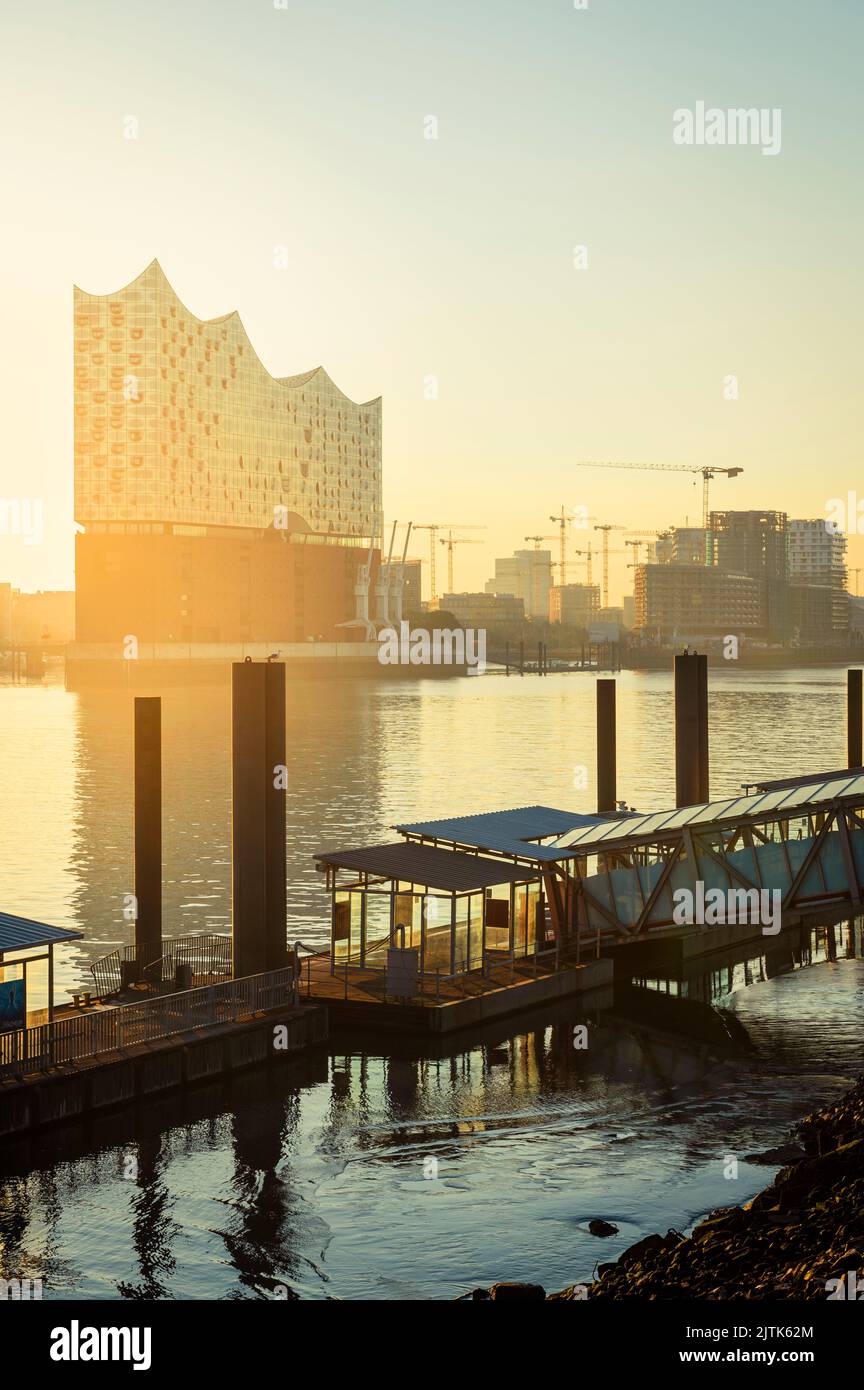 Amanecer en el Elbphilharmonie, Hafencity y un muelle de ferry en el río Elba en el puerto de Hamburgo, Alemania Foto de stock