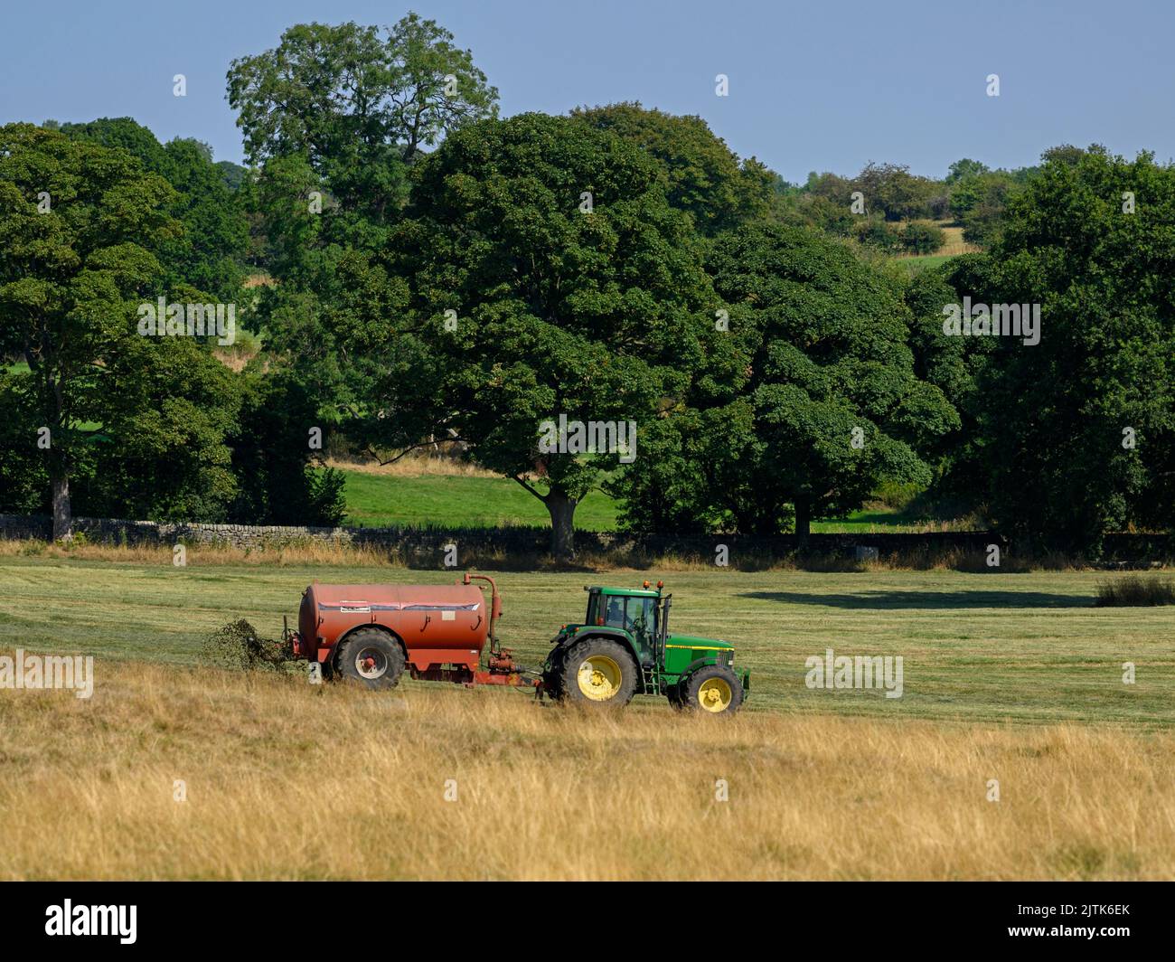 Agricultor trabajando con tractor de conducción y tanque de fertilizante cilíndrico rociando con purina descarga en campo agrícola pasto - Yorkshire, Inglaterra, Reino Unido Foto de stock