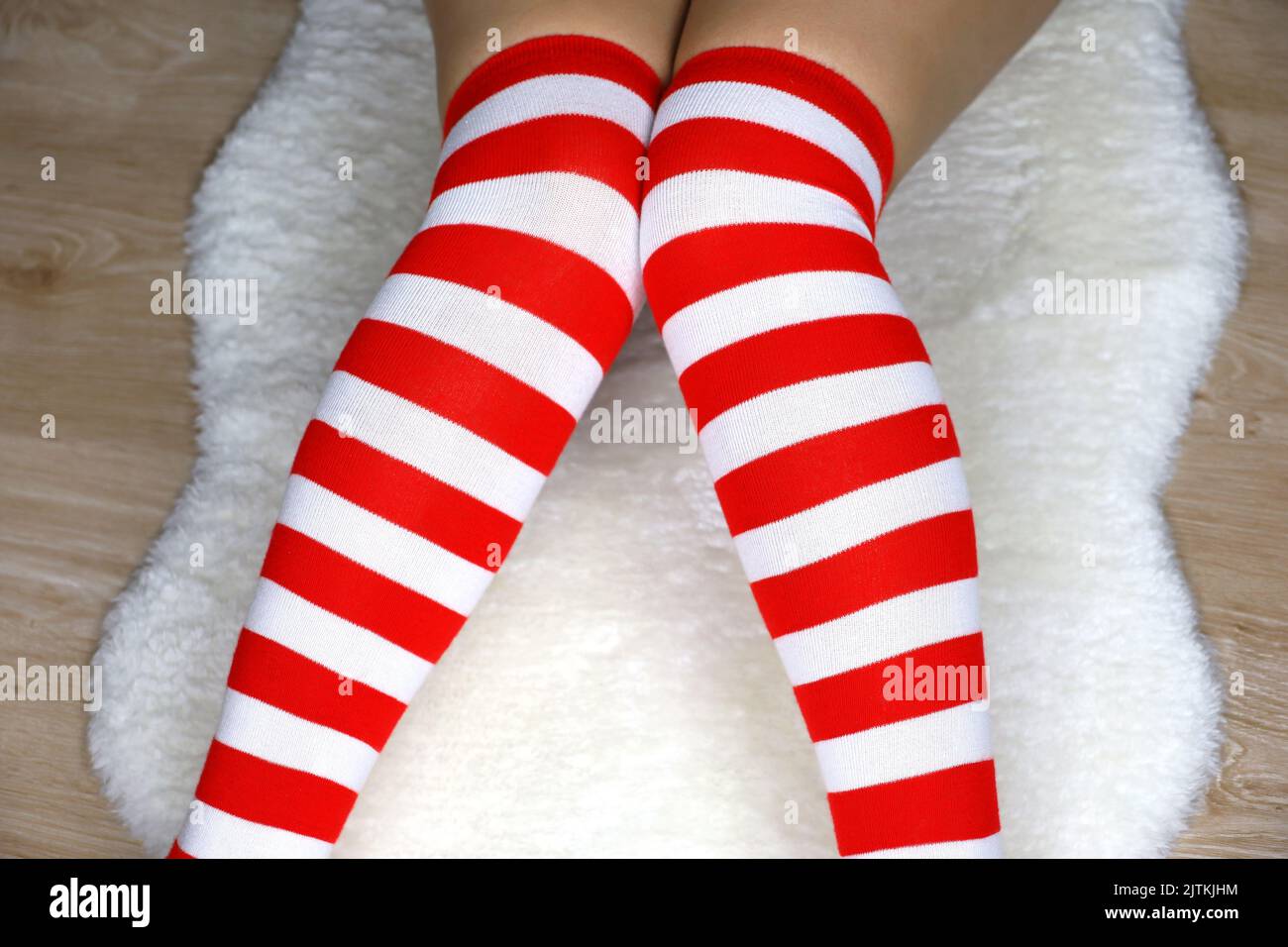 Piernas de niña en Navidad calcetines de rodilla sentados sobre alfombra de piel blanca sobre piso de madera. Traje femenino para la celebración de Año Nuevo Foto de stock