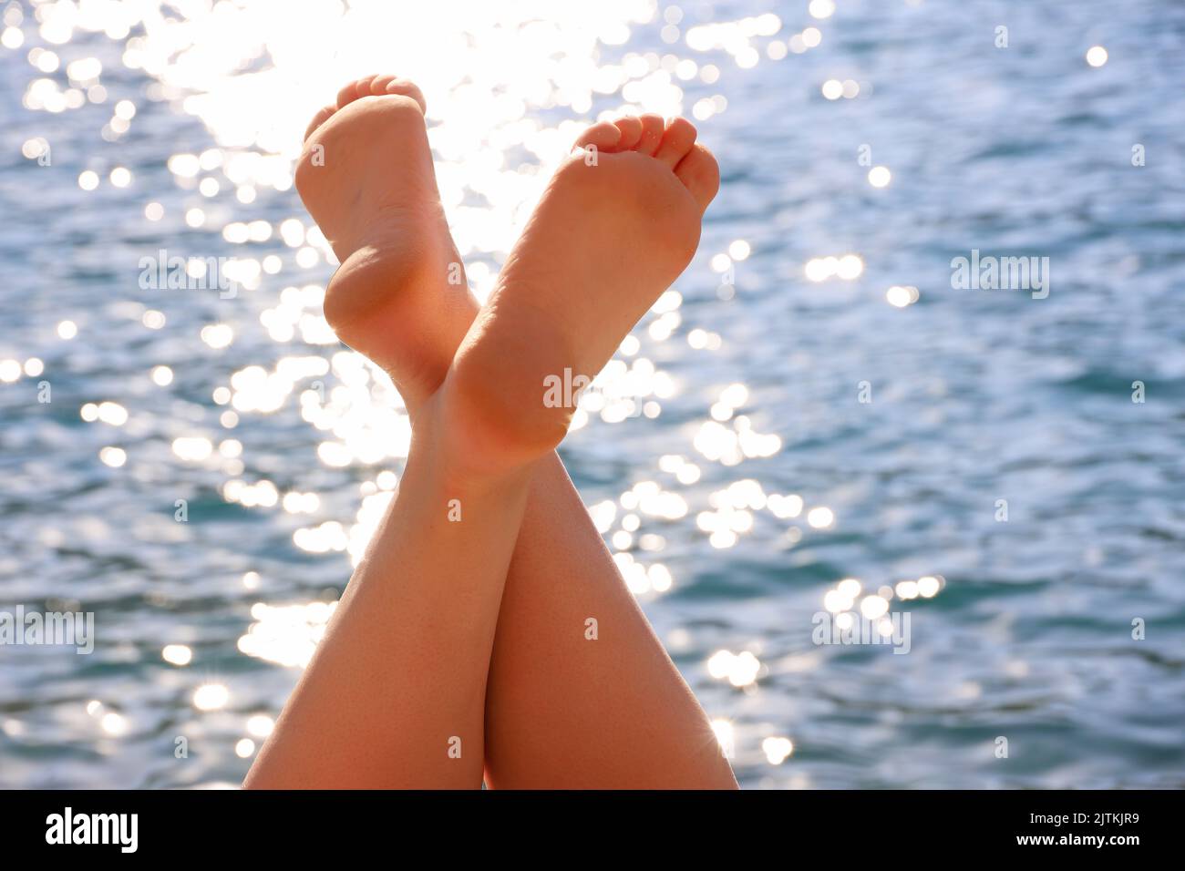 Primer plano de las piernas cruzadas femeninas sobre fondo azul marino. Broncearse, relajarse en la playa y vacaciones de verano Foto de stock