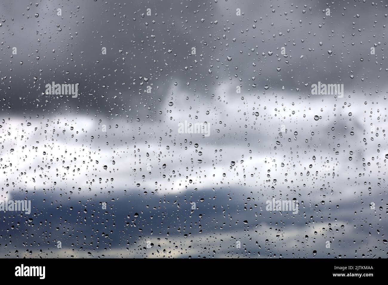 Gotas de lluvia sobre el cristal de la ventana sobre un fondo borroso del cielo con nubes de tormenta. Hermosas gotas de agua, tiempo lluvioso Foto de stock