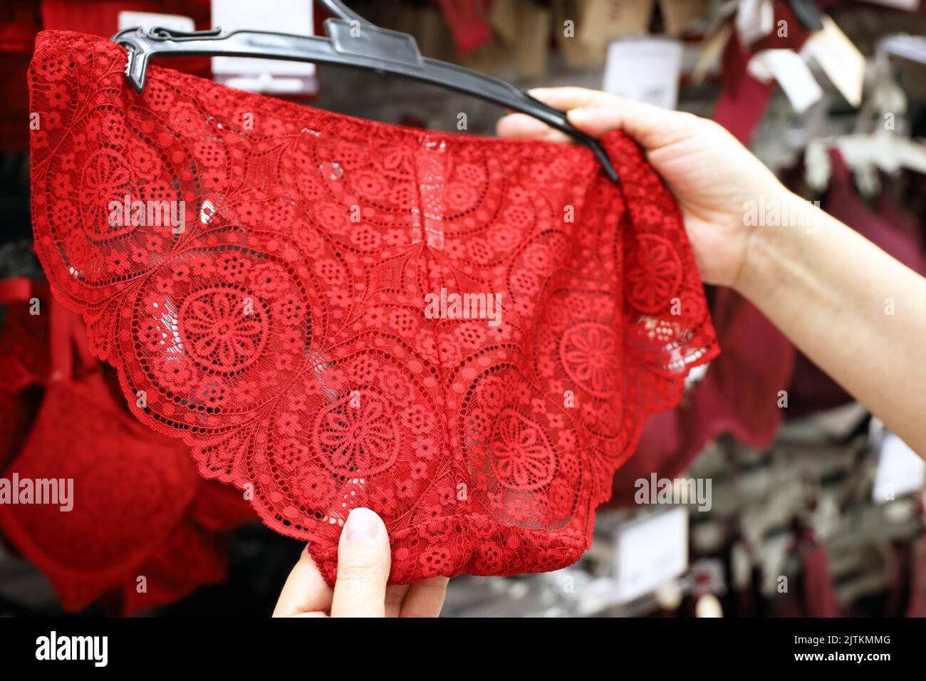 Mujer elige bragas con encaje rojo en tienda de lencería. Moda femenina, ropa interior de diferentes tamaños Foto de stock