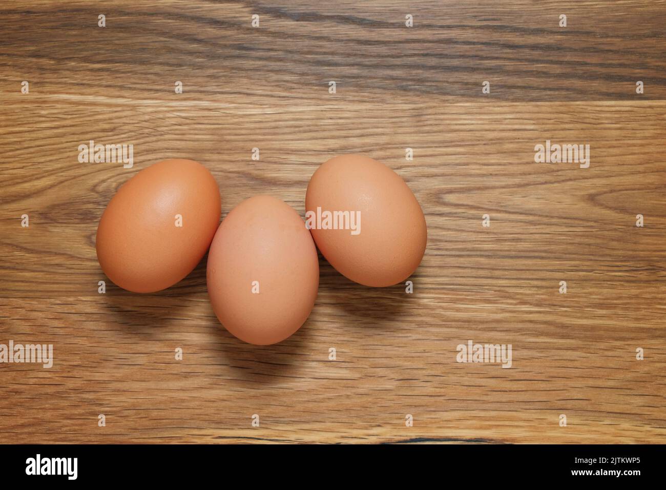 Tres huevos de gallinas marrón disparó desde arriba en una mesa de madera Foto de stock