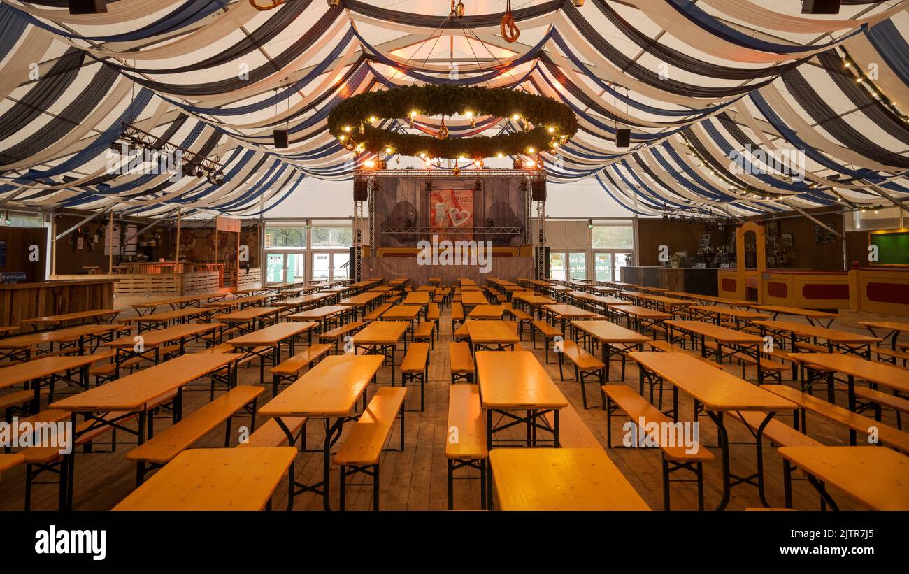 Tienda de cerveza bávara vacía con bancos de cerveza, escenario y festivo techo a rayas blanco y azul Foto de stock