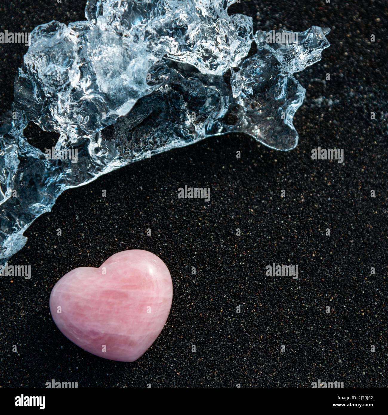 Hielo y corazón de cuarzo rosa sobre arena negra en Islandia, fondo de aventura romántica Foto de stock