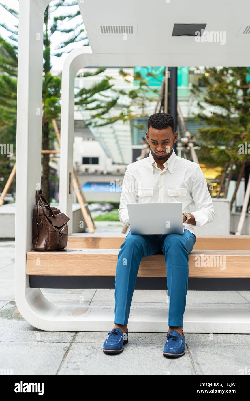 Retrato de un hombre negro joven y elegante con un ordenador portátil en la ciudad Foto de stock