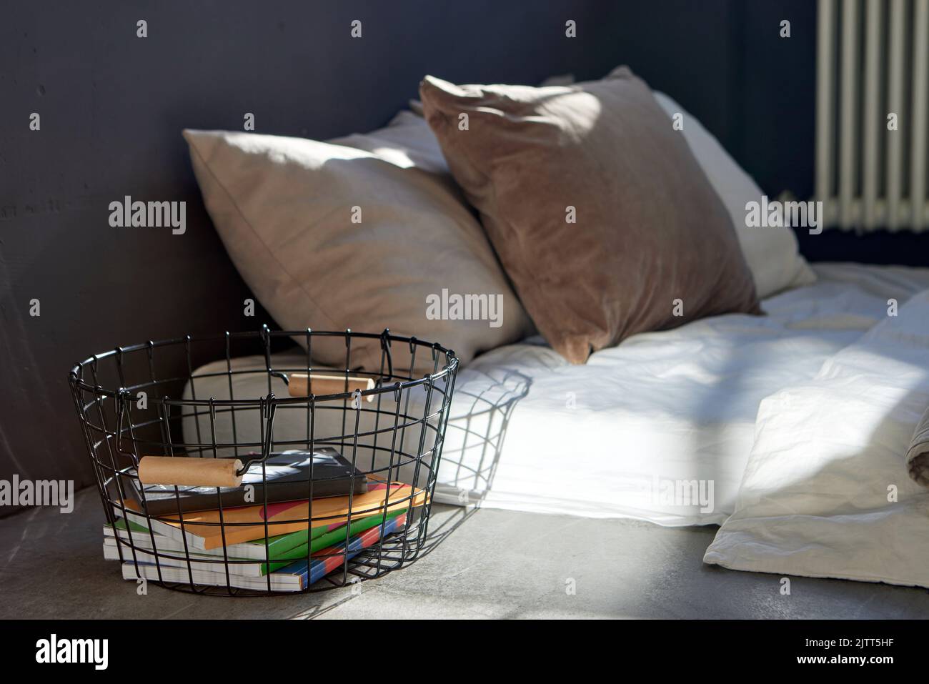 Cesta de metal con cuadernos colocados cerca de la cama en el apartamento Foto de stock
