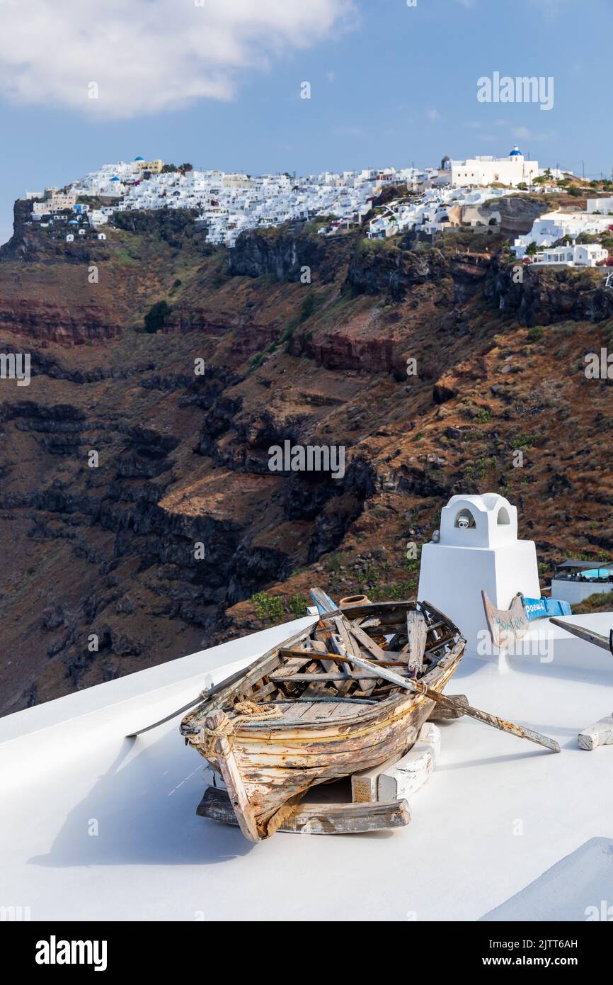 Antiguo barco de remo de madera erosionada se muestra en un tejado en Firostefani con Imerovigil en el fondo, Santorini, islas Cícladas, Grecia, Europa Foto de stock