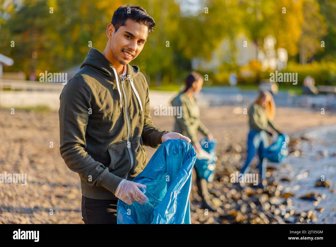 El hombre recoge la basura en una bolsa con un grupo de voluntarios el día soleado Foto de stock