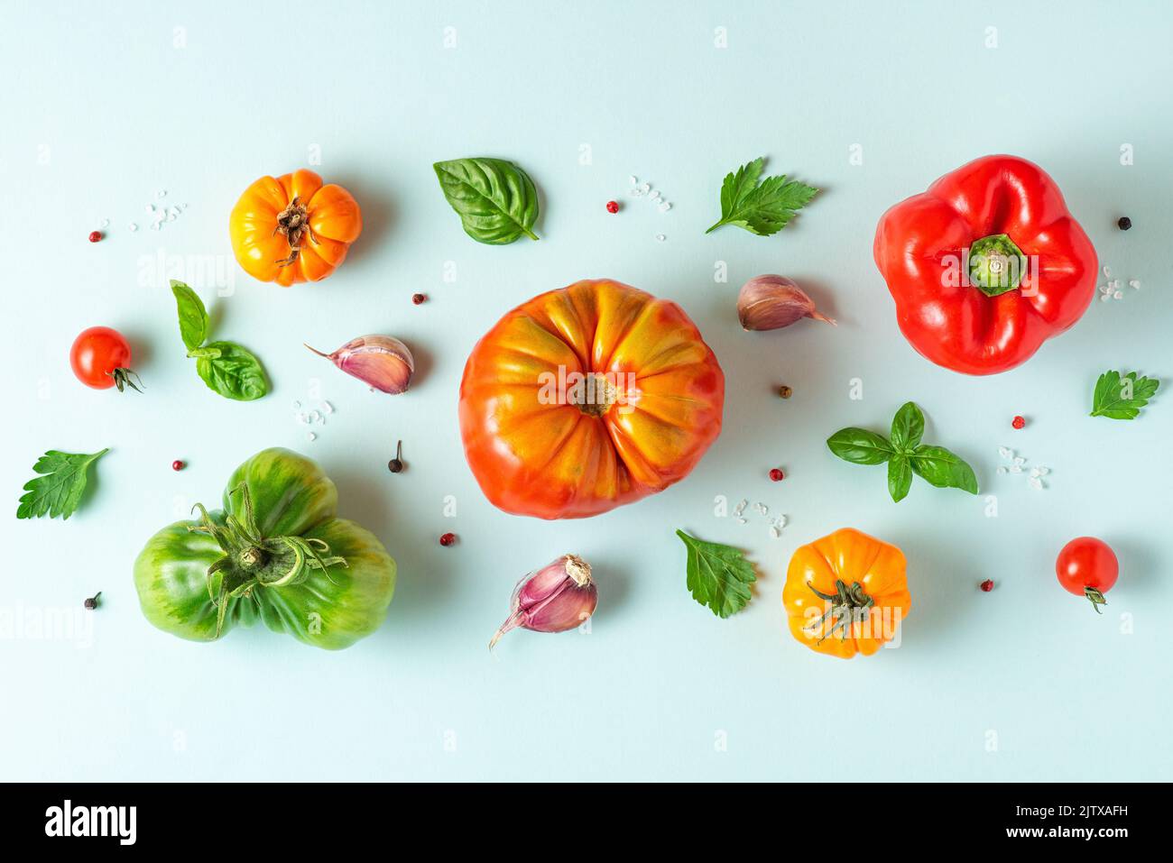 Composición de los alimentos. Tomates, albahaca, ajo y pimienta sobre fondo azul pastel. Colocación plana. Vista superior. El patrón de las verduras Foto de stock