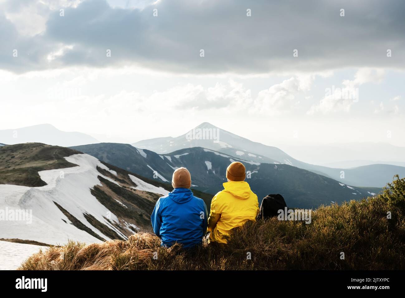 Dos turistas se sientan en el borde de un pico de montaña. Montañas con niebla al fondo. Cárpatos ucranianos, Ucrania. Fotografía de paisajes Foto de stock