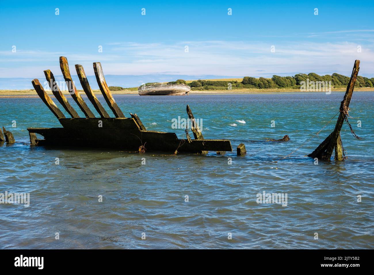Restos de casco antiguo de madera de un naufragio con un barco naufragado más completo a través de la bahía. Traeth Dulas, Isla de Anglesey, Gales del Norte, Reino Unido, Gran Bretaña Foto de stock