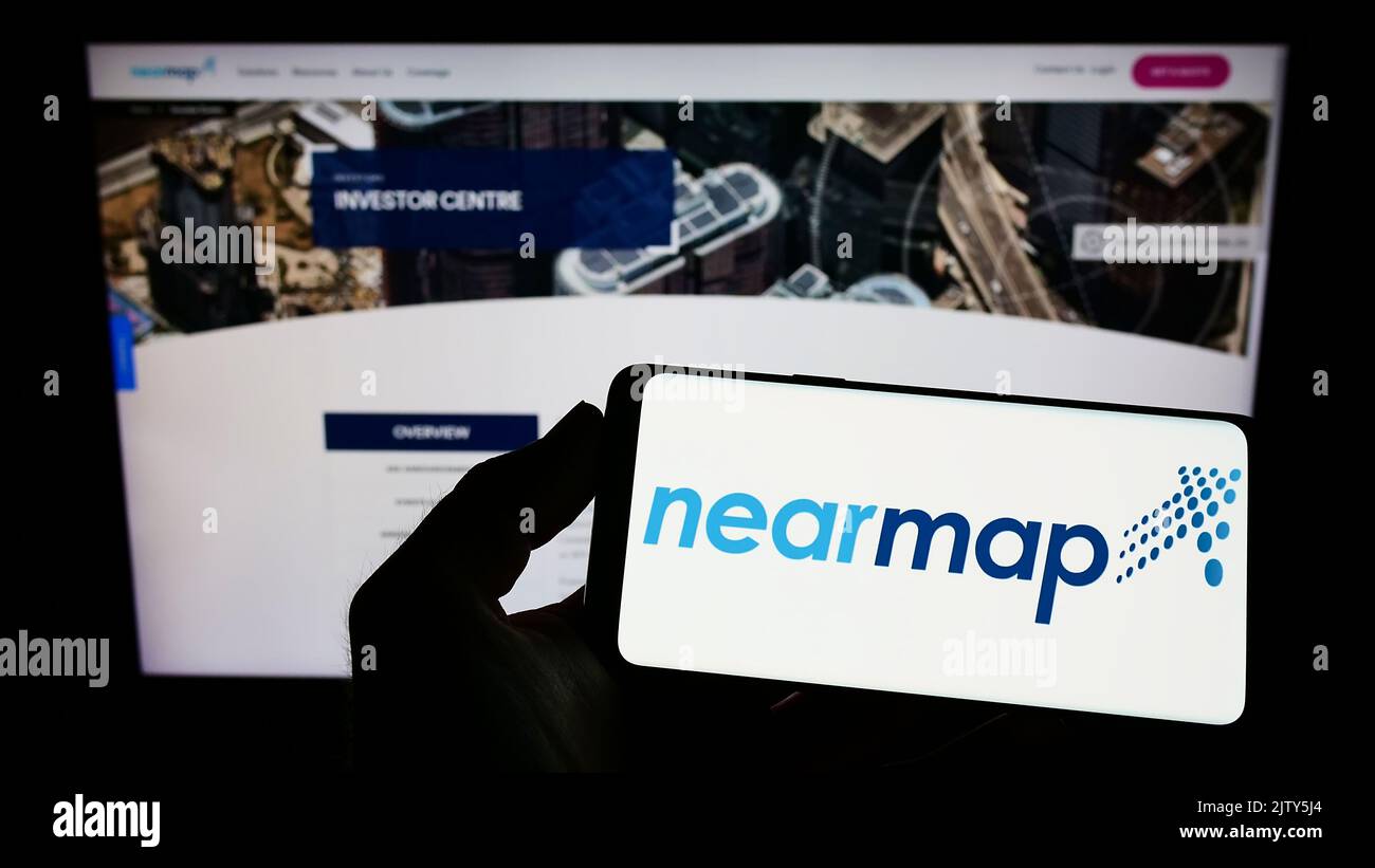Persona que sostiene un smartphone con el logotipo de la compañía de imágenes aéreas Nearmap Limited en la pantalla delante del sitio web. Enfoque la pantalla del teléfono. Foto de stock