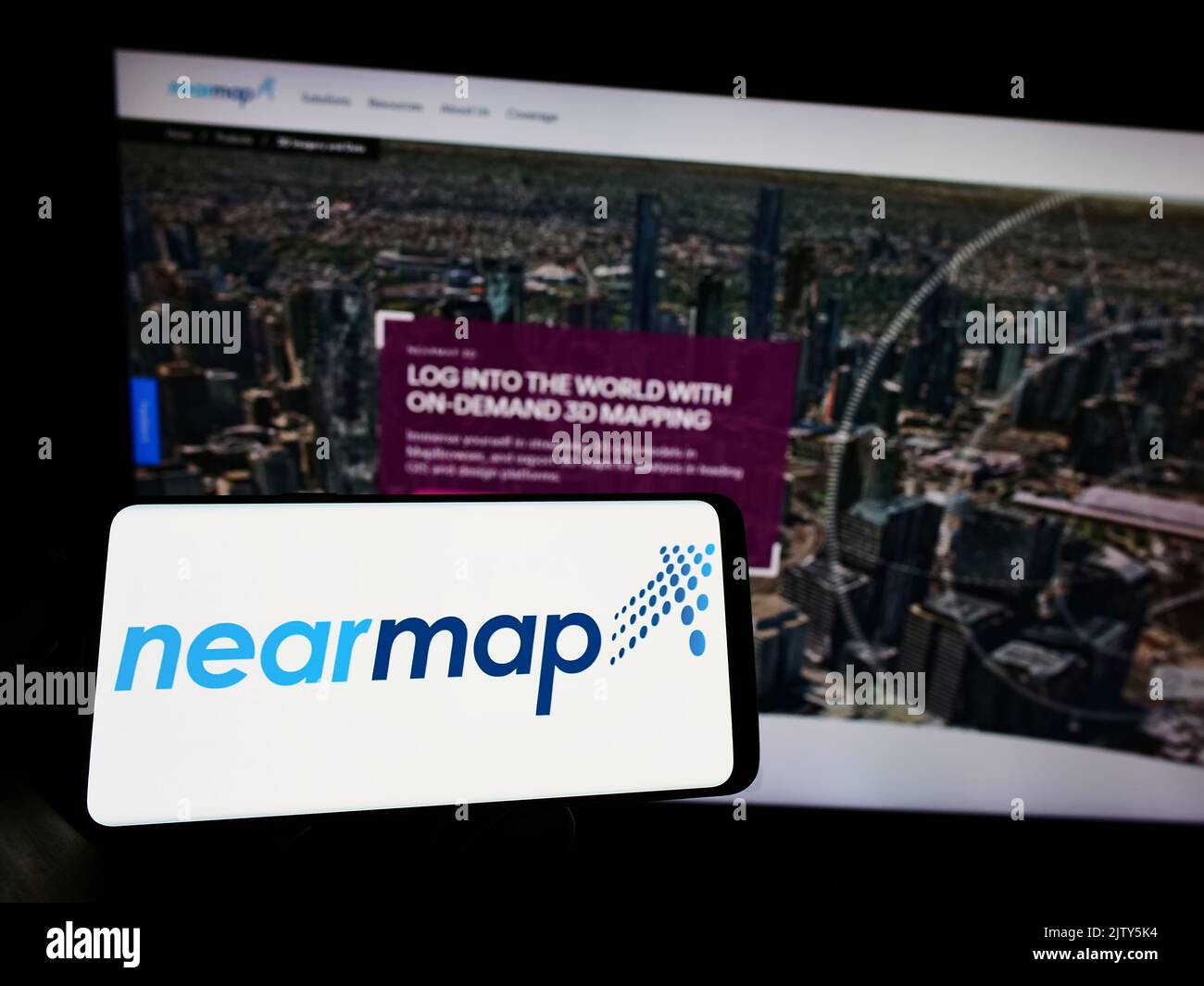 Persona que sostiene el teléfono celular con el logotipo de la compañía de imágenes aéreas Nearmap Limited en la pantalla delante de la página web del negocio. Enfoque la pantalla del teléfono. Foto de stock