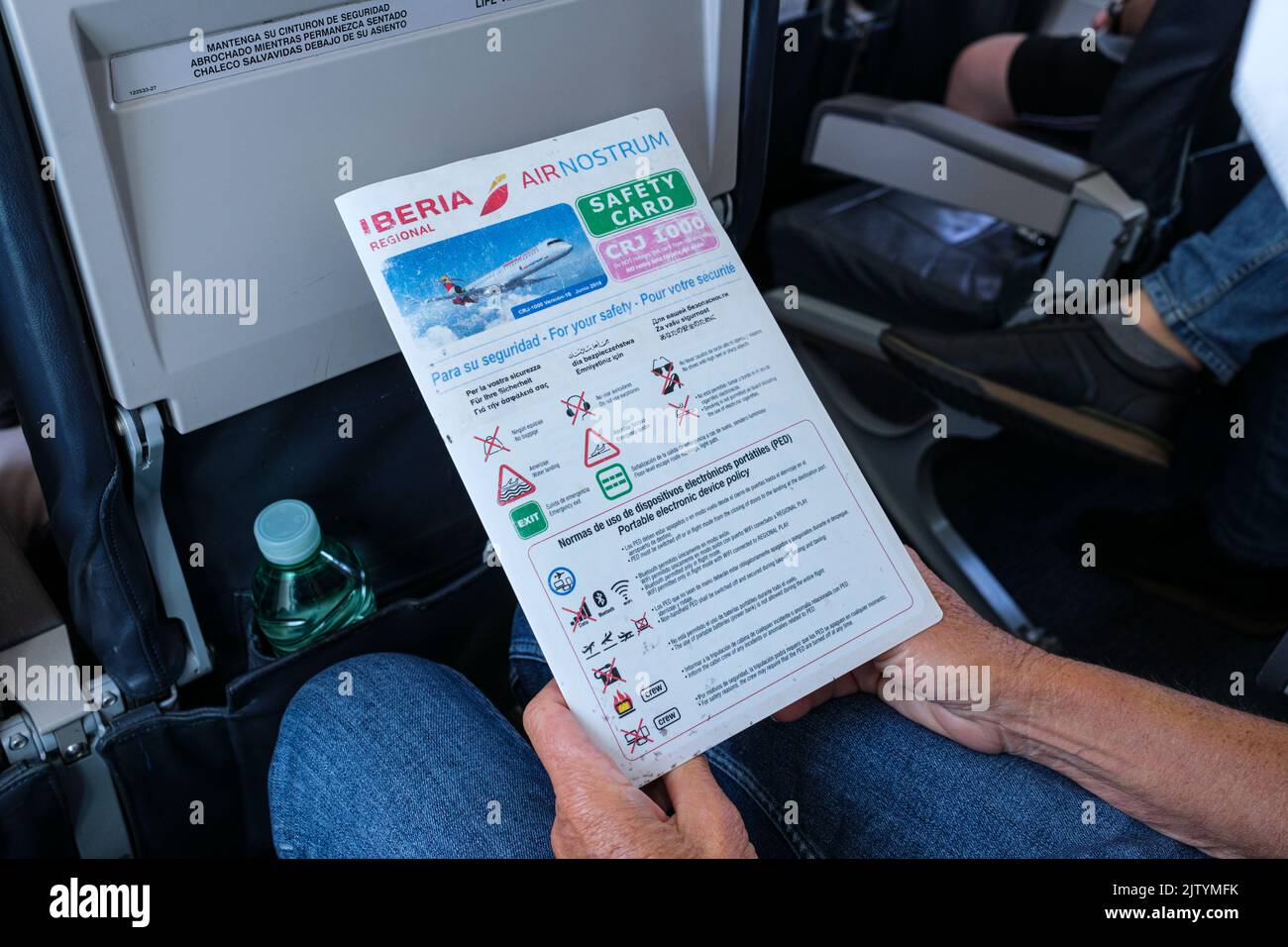Pasajero que lee la información de la tarjeta de seguridad mientras viaja en avión desde Madrid a granada, en un avión Bombardier CRJ1000, España Foto de stock