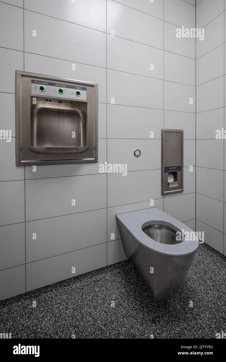 Interior de un nuevo y moderno baño público limpio con azulejos blancos y cuenco de acero inoxidable Foto de stock