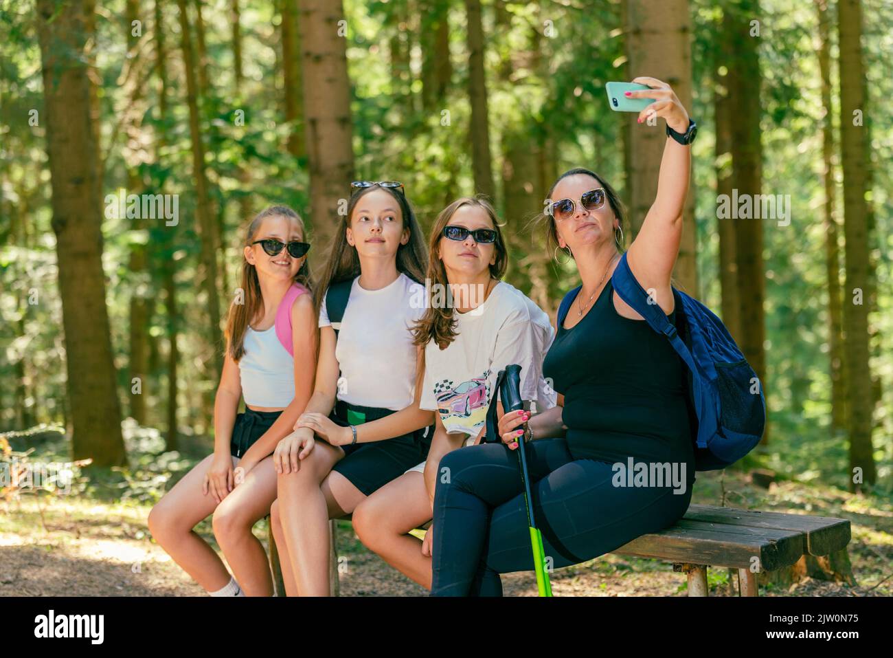 Los montañeros toman selfie con el teléfono en un banco de madera. Bosque en el fondo Foto de stock