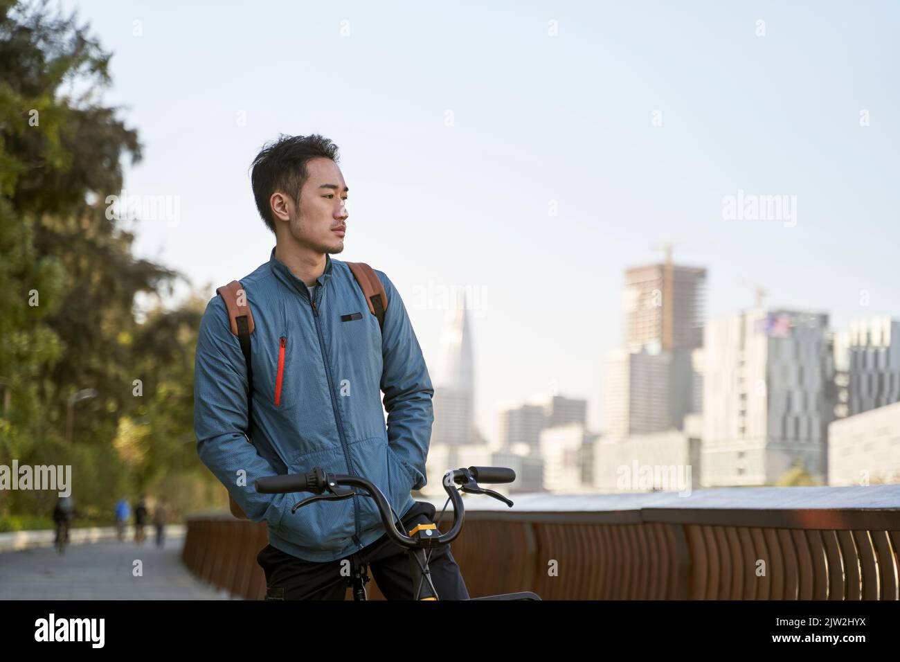 hombre adulto joven asiático sentado en su bicicleta perdido en el pensamiento en el parque de la ciudad Foto de stock