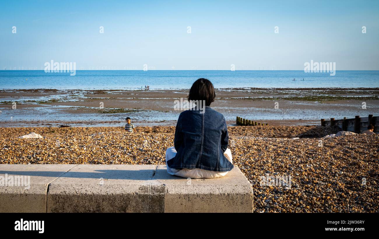 Una mujer se sienta con las piernas cruzadas para meditar en la pared del mar en Worthing, West Sussex, Reino Unido. Foto de stock