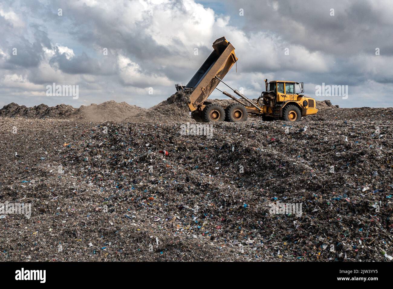 Un camión volador en un gran vertedero de gestión de residuos que descarga basura en una imagen de problema medioambiental Foto de stock