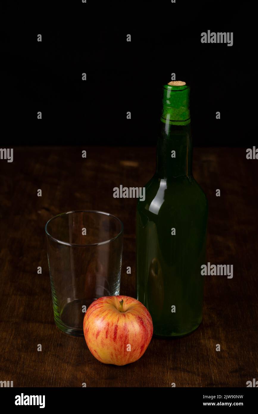 Botella de sidra junto a un vaso vacío y una manzana. Foto de stock