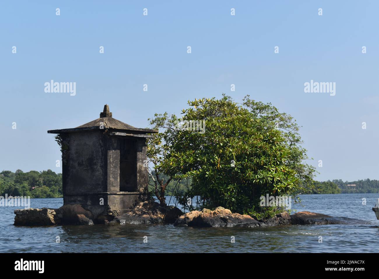 El islote más pequeño del lago Madu Ganga se llama “Satha Paha Doowa”. “Paha” se traduce como “cinco”, mientras que “Satha” significa “centavo”. Según la tradición local, el islote había sido comprado una vez por cinco centavos. Pero otros dicen, él consiguió su nombre debido a la forma o el tamaño pequeño que se asemeja apenas a una moneda pequeña. Sin embargo, FICE-CENT-ISLAND es lo suficientemente grande como para llevar un templo. El santuario está dedicado a Kataragama, una deidad venerada por budistas cingaleses e hindúes tamil y animistas de Weddah por igual. En cierto modo, es un Devale, un santuario budista para una deidad hindú. Sri Lanka. Foto de stock