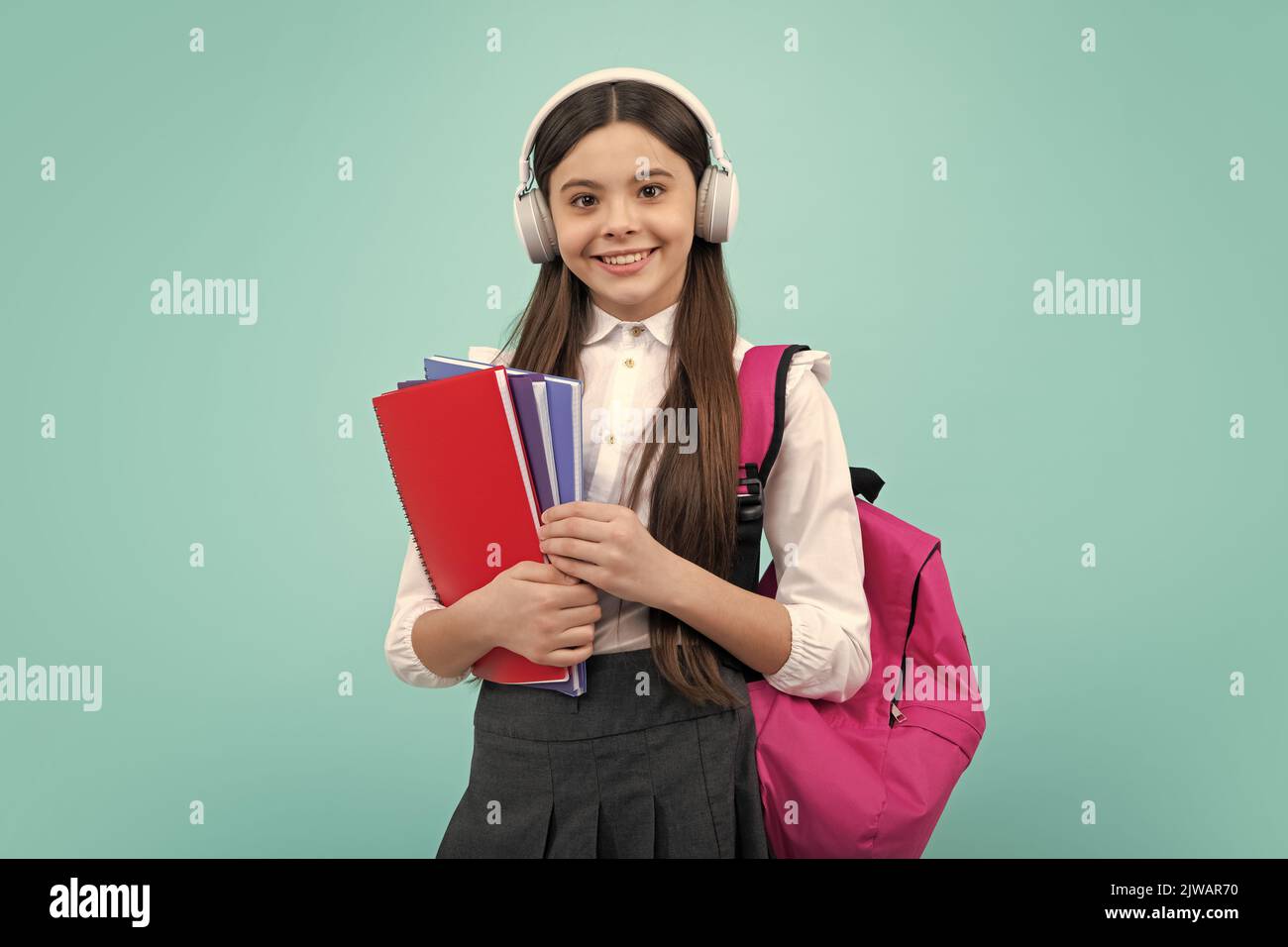 Colegiala, adolescente niña de estilo de vida estudiante en los auriculares sostener libros sobre fondo de estudio aislado azul. Concepto de educación escolar y musical. Foto de stock