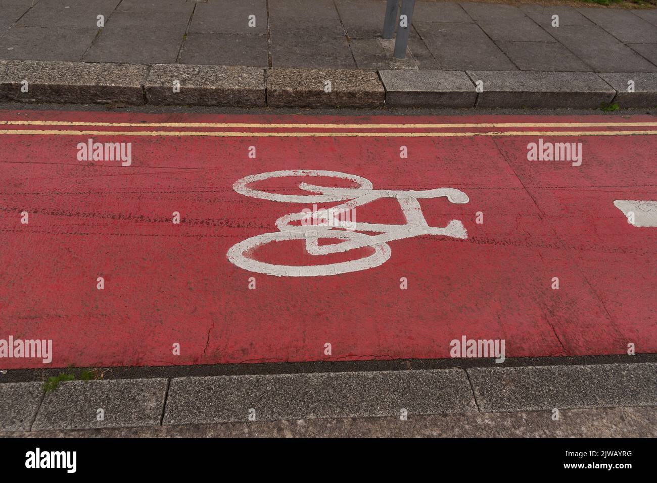 Plymouth, Devon, Inglaterra, Reino Unido. 2022. Bicicleta pintada de blanco sobre la superficie de la carretera de color rojo a lo largo de una carretera de la ciudad que muestra la curva desplegable y doble línea amarilla Foto de stock