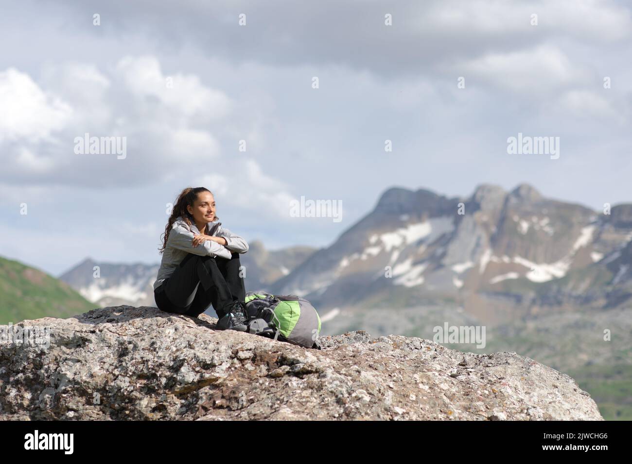 Excursionista en la cima de una montaña contemplando vistas sentado en una roca Foto de stock