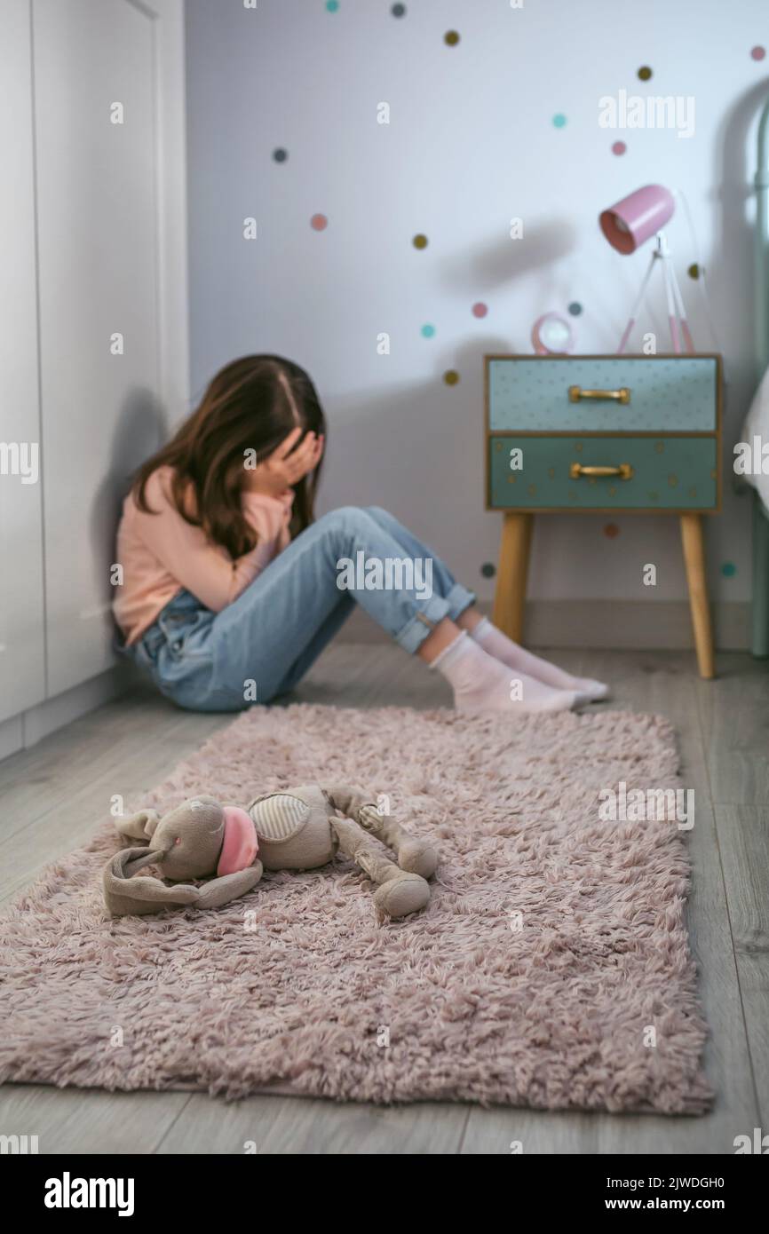 Niña triste con ansiedad sentada en el piso de su dormitorio con juguete de peluche acostado Foto de stock