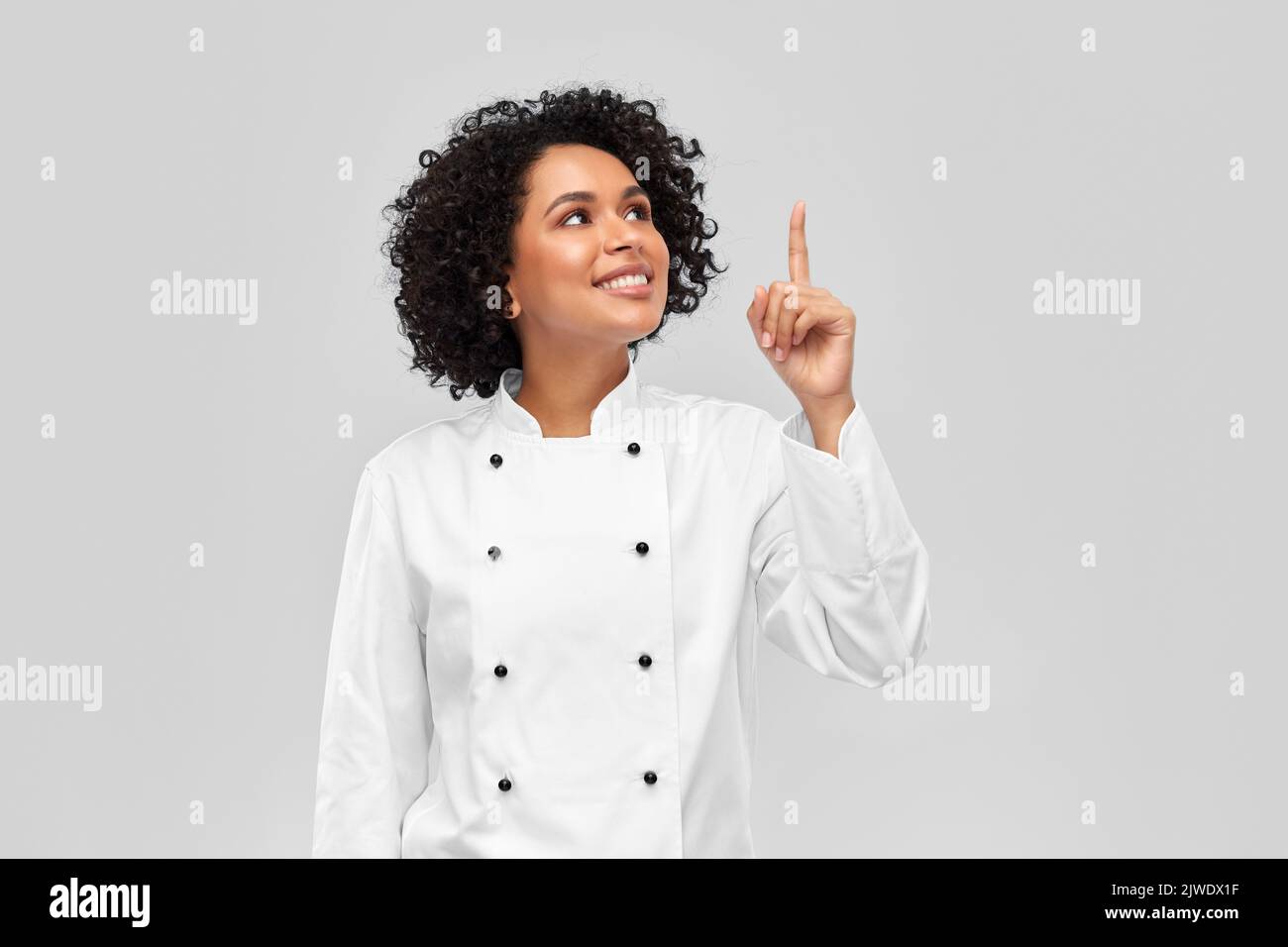 chef sonriente en chaqueta señalando con el dedo hacia arriba Foto de stock
