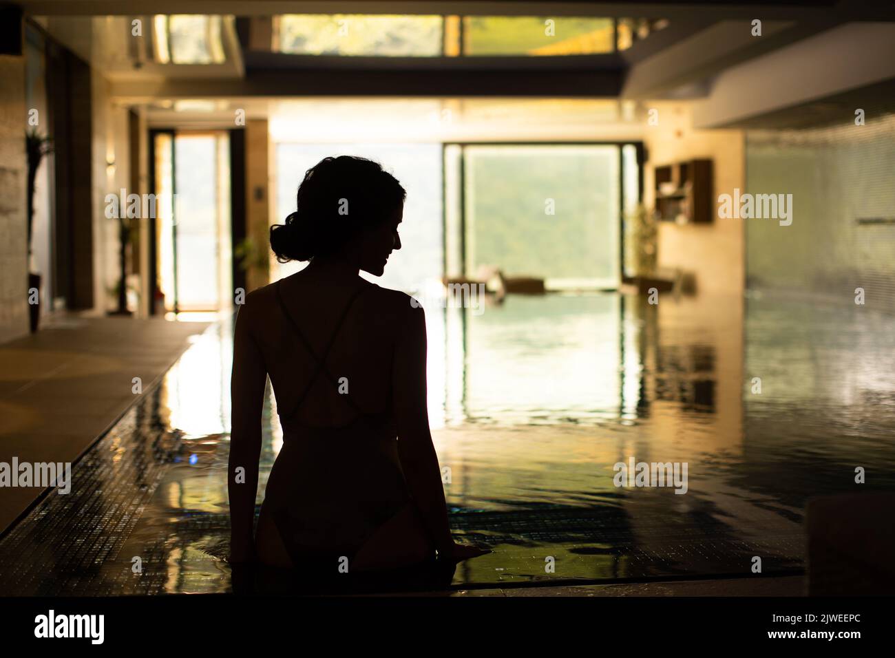 Vista trasera de una mujer joven y bonita que se estaba relajando junto a la piscina Foto de stock