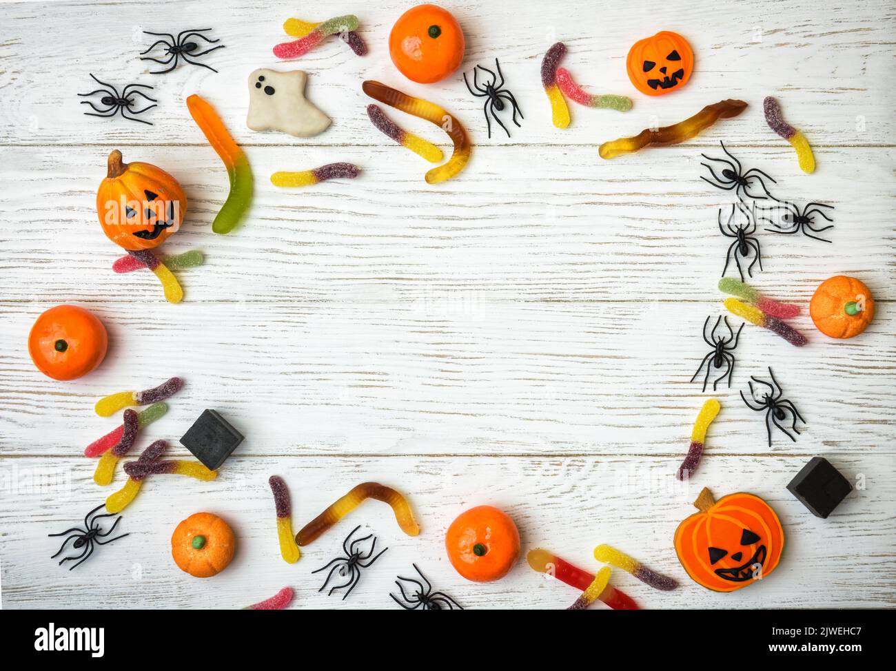 Dulces y decoraciones de Halloween sobre fondo de madera blanca. Vista superior del marco de Halloween con galletas, fantasma, arañas y dulces sobre una mesa de madera, la plana Foto de stock