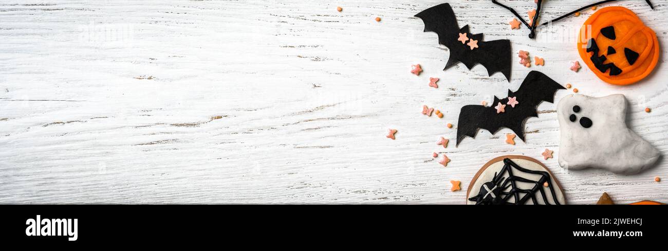 Tabla de Halloween de fondo con dulces y decoraciones. Vista superior de las galletas de Halloween, fantasmas y murciélagos en la mesa de madera blanca y el espacio, plano. Panor Foto de stock