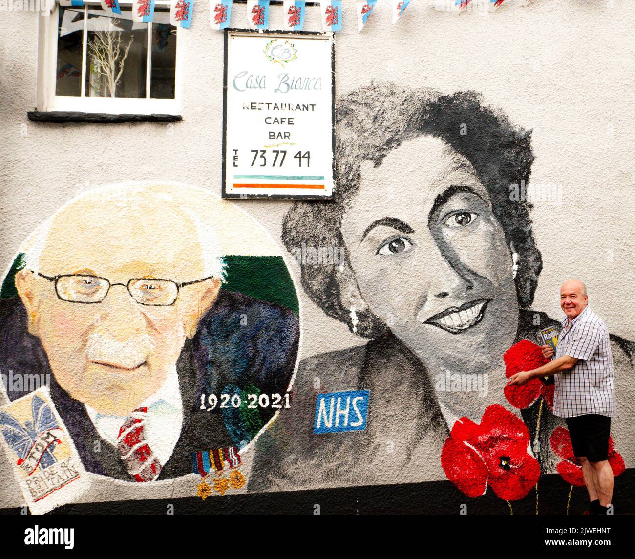 Paul Cable, quiosco de prensa y artista local de Abergavenny, está al lado de un mural que pintó en la ciudad, con el capitán Sir Tom Moore y Dame Vera Lynn. Foto de stock