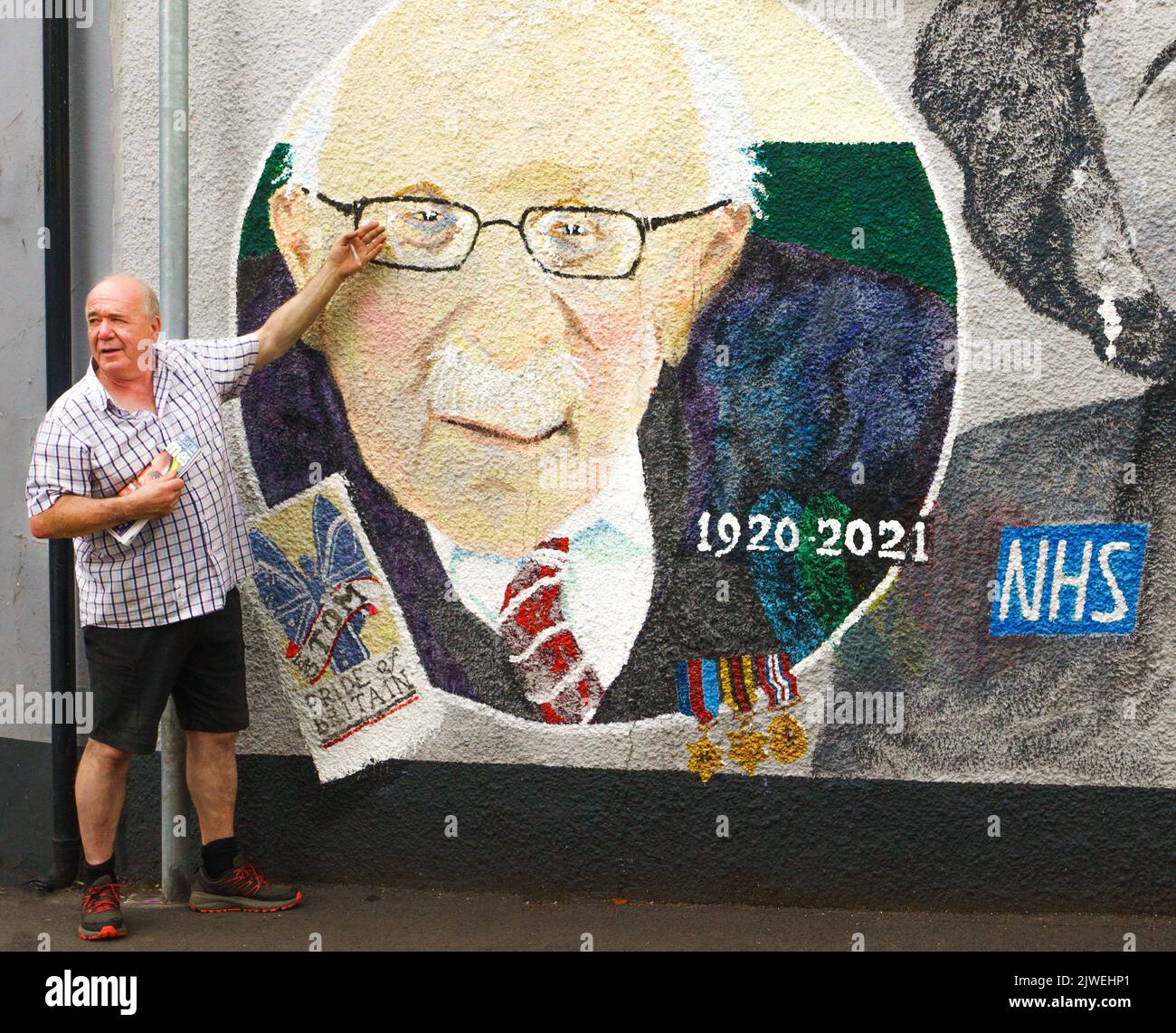 Paul Cable, quiosco de prensa y artista local de Abergavenny, está al lado de un mural que pintó en la ciudad, con el capitán Sir Tom Moore y Dame Vera Lynn. Foto de stock