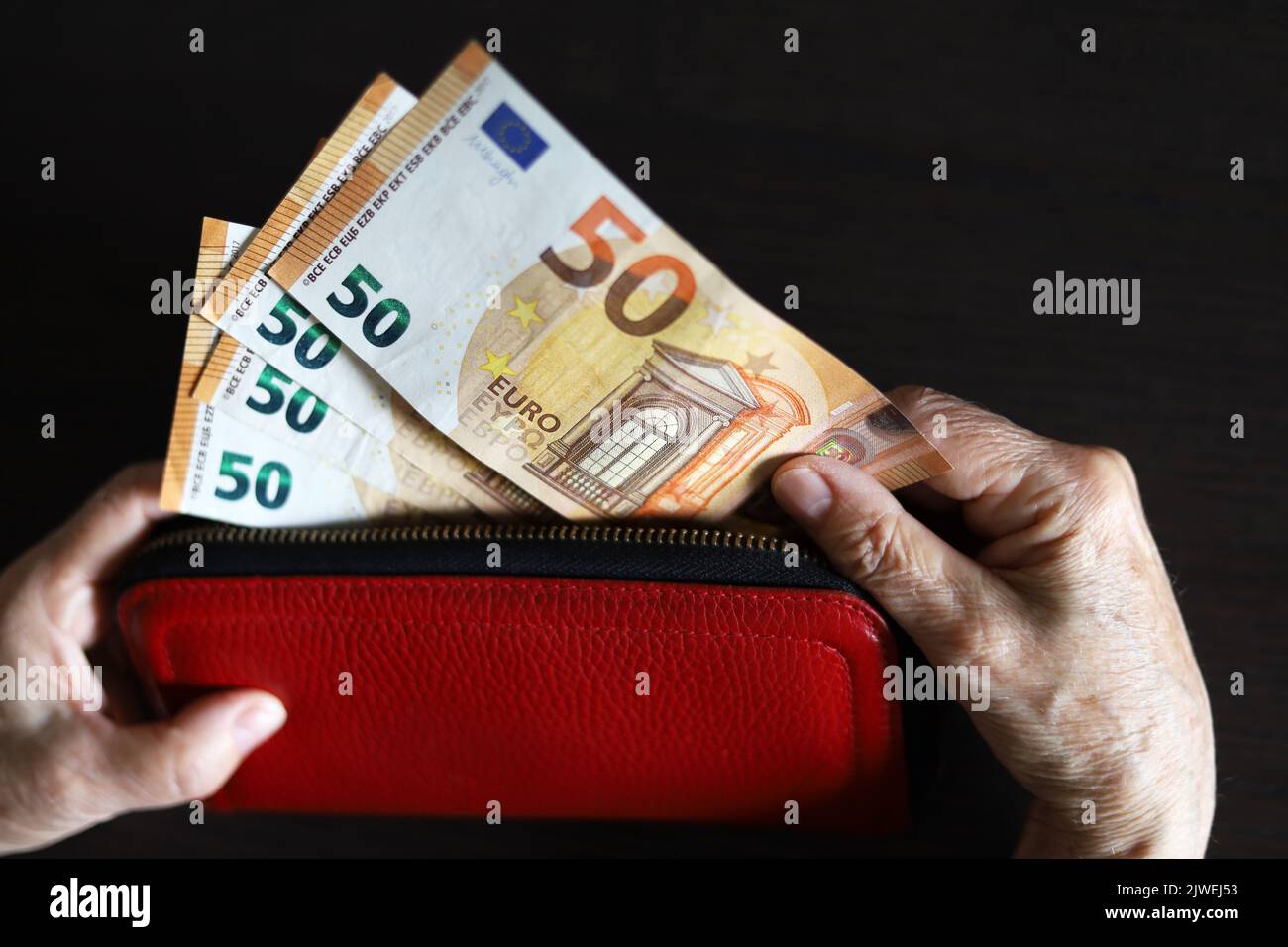 Billetes en euros con las manos arrugadas, una mujer mayor saca dinero de la cartera roja. Concepto de pensiones y asistencia, ahorro, jubilación en la UE Foto de stock