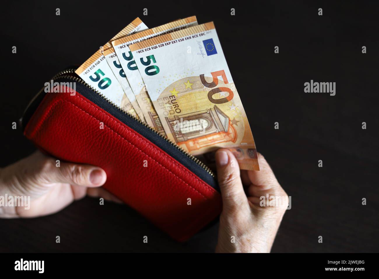 Billetes en euros con las manos arrugadas, una mujer mayor saca dinero de la cartera roja. Concepto de pensiones y asistencia, ahorro, jubilación en la UE Foto de stock