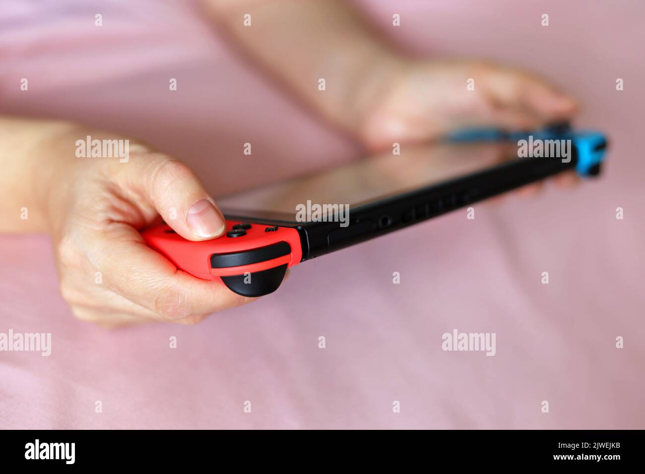Mujer jugando en la consola de mano acostada en una cama, enfoque selectivo en una mano Foto de stock