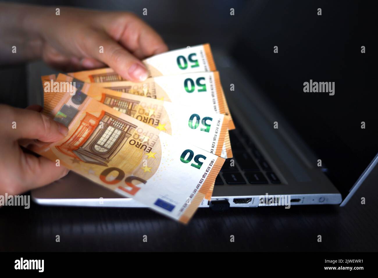 Billetes en euros en manos femeninas sobre el fondo del ordenador portátil. Mujer contando dinero, concepto de salarios o bonos Foto de stock