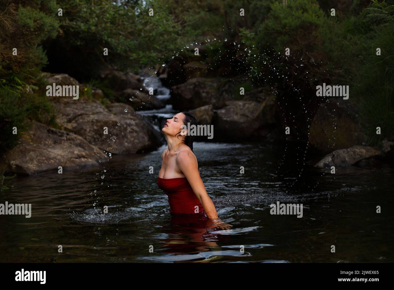 Una hermosa mujer joven con un vestido rojo enfriándose en un río. Foto de stock