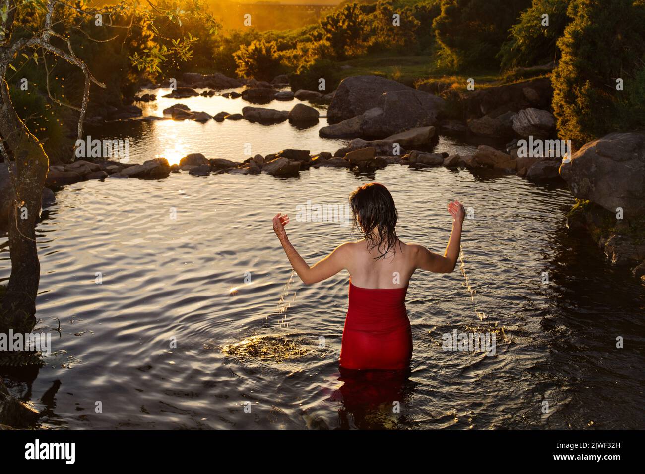 Una hermosa mujer joven con un vestido rojo enfriándose en un río Foto de stock